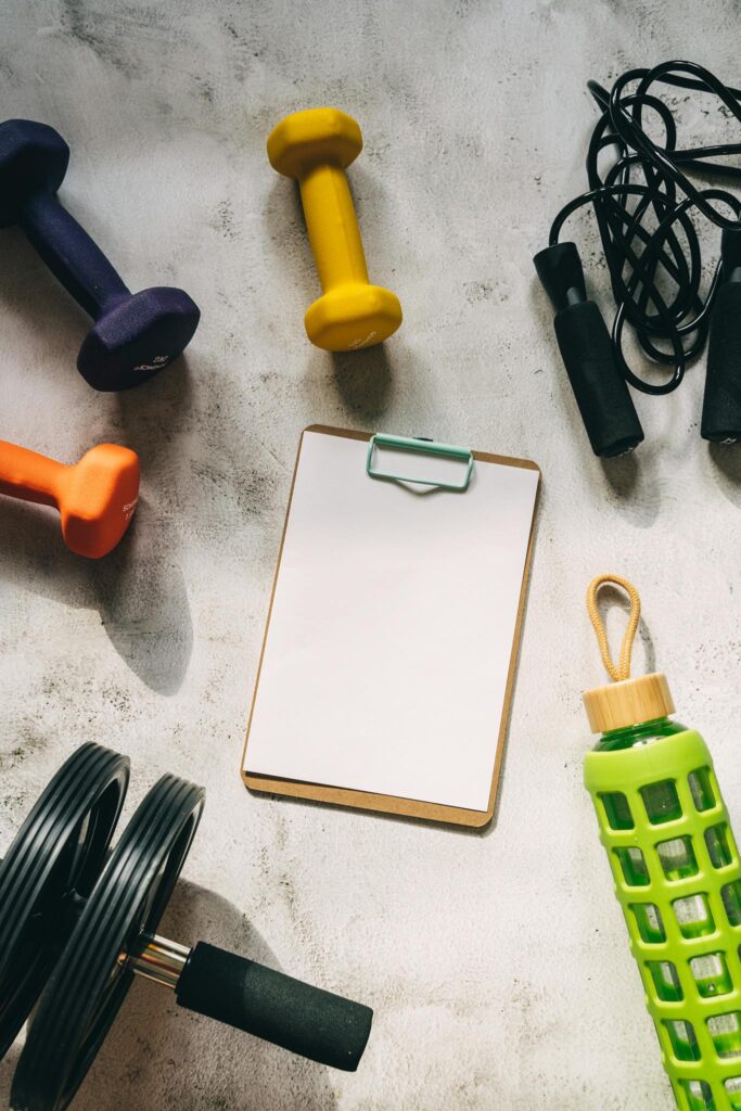 Flat lay of colorful dumbbells, fitness gear, and blank clipboard for workout planning.